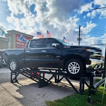 Black pickup truck displayed on a ramp with American flags.