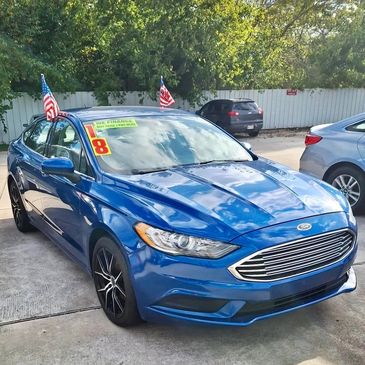 Blue Ford sedan with American flags and financing signs on windshield.