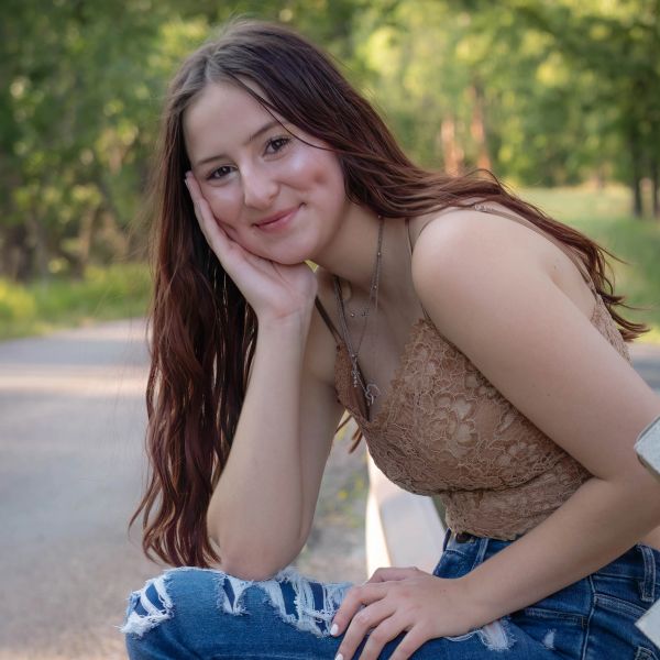 Young woman smiling, leaning her head on her hand outdoors.