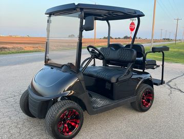 Black golf cart with red-striped wheels parked on a rural road at sunset.