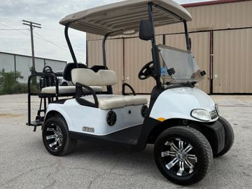 White EZGO golf cart with beige seats and black rims parked outside.