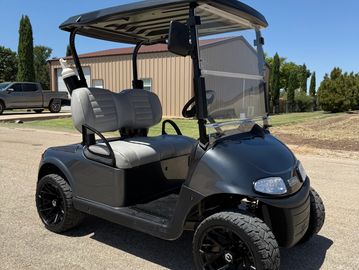 Sleek black golf cart with gray seats parked on a sunny day.