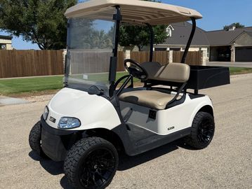 White golf cart with black wheels parked on a sunny street.