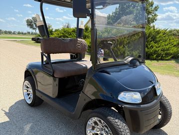 Black golf cart with shiny chrome wheels parked on a sunny road.