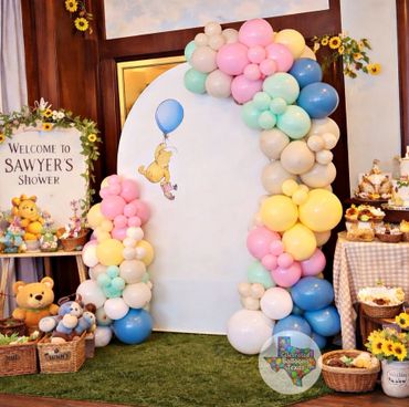 Colorful balloon arch at a baby shower with Winnie the Pooh theme.