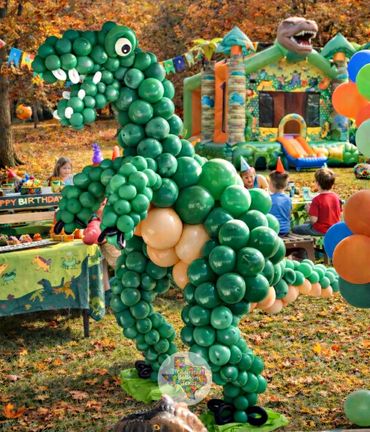 A large dinosaur made of green balloons at a colorful outdoor birthday party.