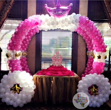 A pink and white balloon arch with a birthday cake setup.
