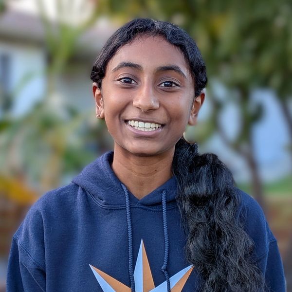 Young person smiling outdoors in a hoodie.