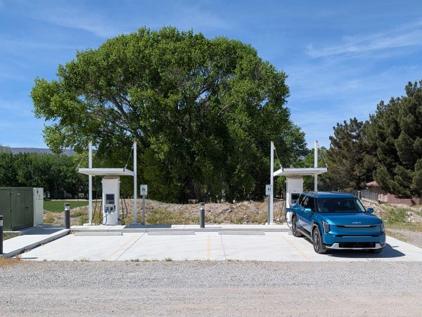 Blue electric vehicle charging at a station with two chargers under clear sky.