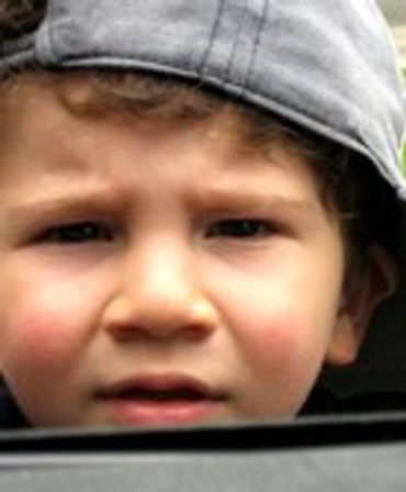 Young child in a baseball cap, looking sad.
