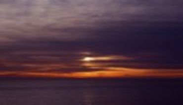 Sunset over water with an orange glow beneath dark clouds