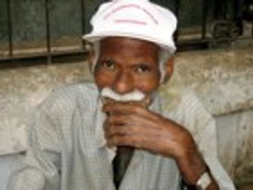 Older man with a white hat and mustache, smoking.