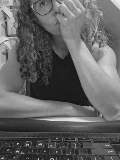 Woman with curly hair and glasses sitting thoughtfully at a desk with a keyboard.
