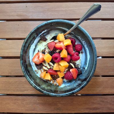 A bowl of yogurt with fresh berries and fruit on a wooden table.