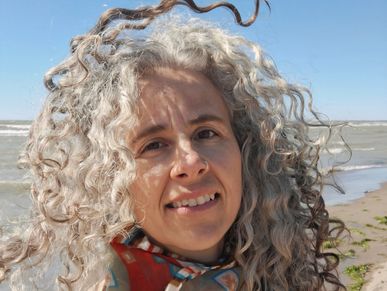 Woman with curly gray hair smiling at the beach on a sunny day.