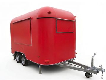 Red mobile food trailer with closed service windows and dual axles.