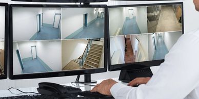 Man monitoring multiple security camera feeds on computer screens.