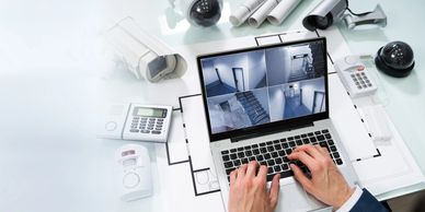 Person monitoring security cameras on a laptop with surveillance equipment nearby.