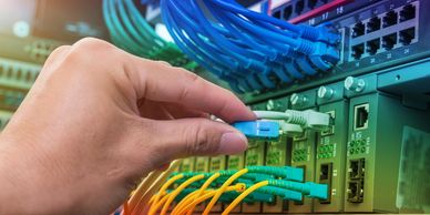 Hand connecting a blue fiber optic cable to a network switch.