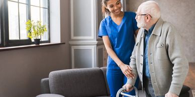 A nurse helps an elderly man with a walker inside a cozy room.
