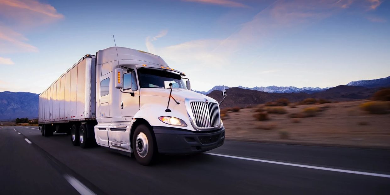 White semi-truck driving on desert highway at sunset.
