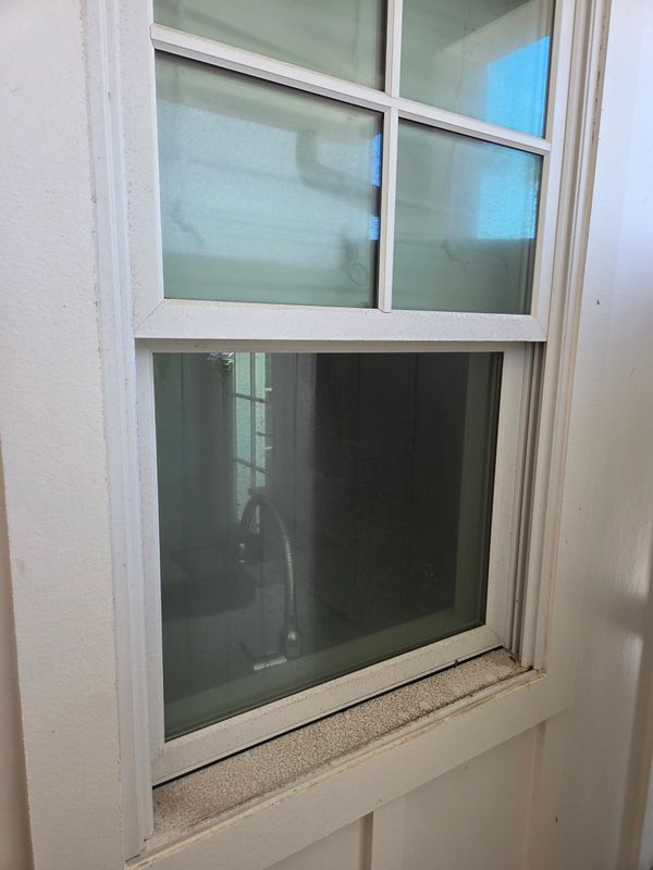 A white-framed window with slightly dirty sill and reflection of a sink inside.