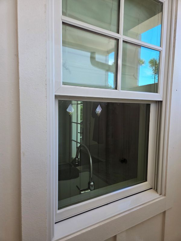 White framed window reflecting indoor faucet and outdoor sky.