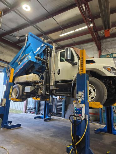 A dump truck lifted on a blue hydraulic lift inside a garage.