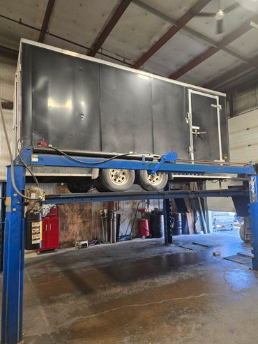Black trailer elevated on a blue hydraulic lift inside a garage.