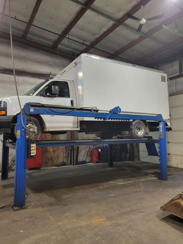 White box truck elevated on a blue vehicle lift inside a garage.