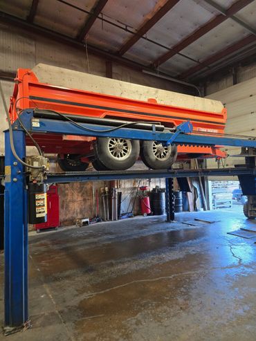 Orange trailer elevated on a blue vehicle lift inside a garage.