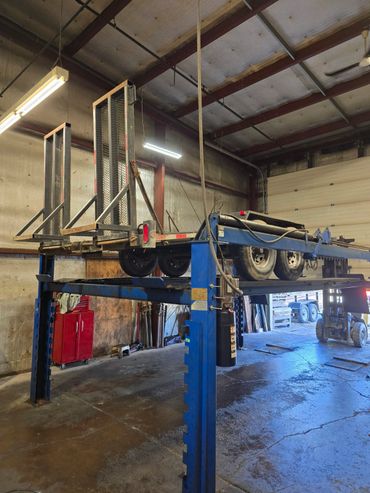 A utility trailer elevated on a blue hydraulic lift inside a garage.