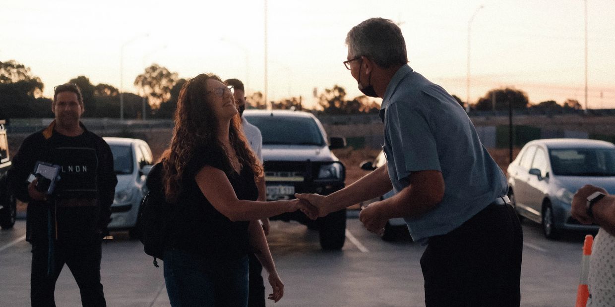 Two people shaking hands outdoors at sunset.