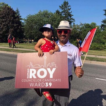 Man holding child and campaign sign for Roy, Ward 39 councillor candidate.