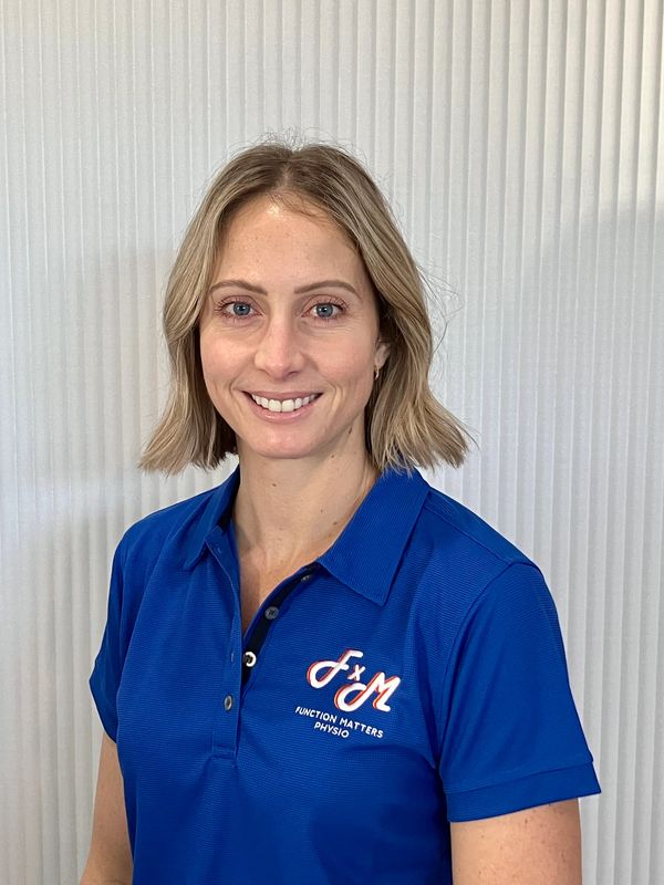 Front of house Glencora is in front of a white clinic wall wearing the royal blue FxM team uniform