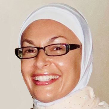 Smiling woman wearing glasses and a white headscarf.