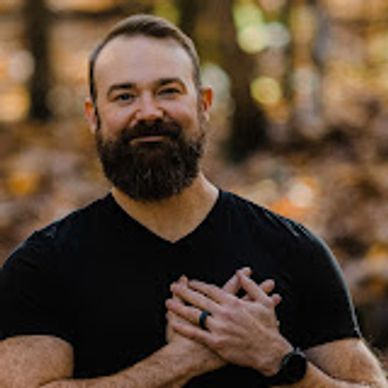 Bearded man in black shirt with hands clasped, outdoors.