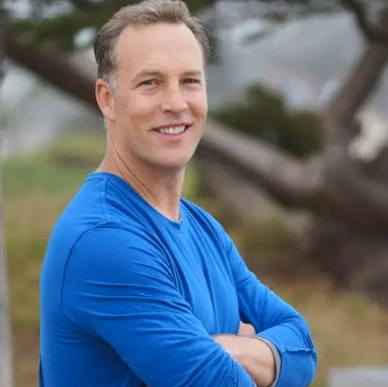 Smiling man in a blue shirt outdoors with arms crossed.