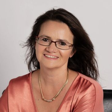 Smiling woman with glasses in a satin blouse.