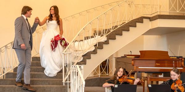 Bride and groom descending stairs with live violinists playing.