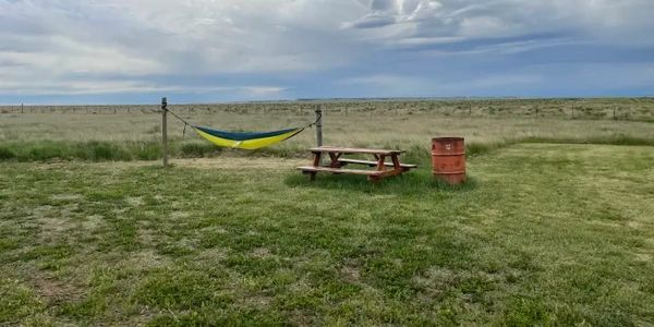 Empty hammock and picnic table in a grassy field under a cloudy sky.