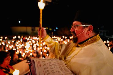 A priest leads a candlelight ceremony at night.