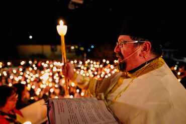 A priest holds a lit candle during a nighttime religious ceremony.