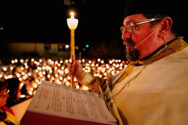 Clergyman reads from a religious book during a candlelit ceremony.