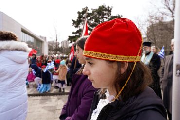 Young girl in traditional red hat at outdoor event.