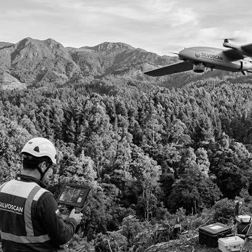 Person operating a drone over a forested mountain area.