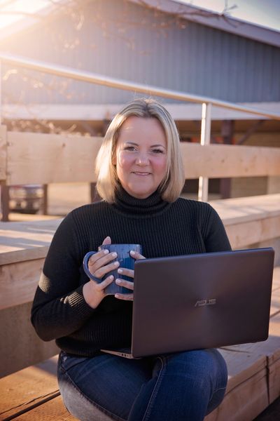 Image of Amanda McCooeye, Child & Youth Care Specialist sitting on a bench with a lap top and a mug
