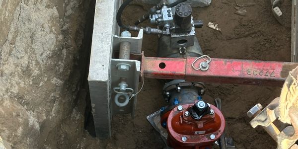 Hydraulic valve setup with red pipe and control mechanism in a soil trench.