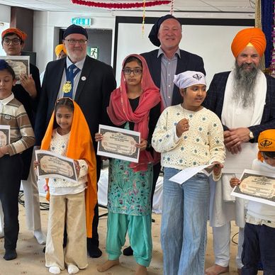 Children and adults holding certificates at a Sikh community event.