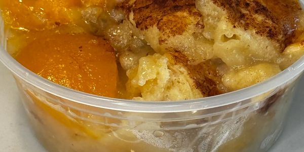 Peach cobbler served in a clear plastic container with a black spoon.